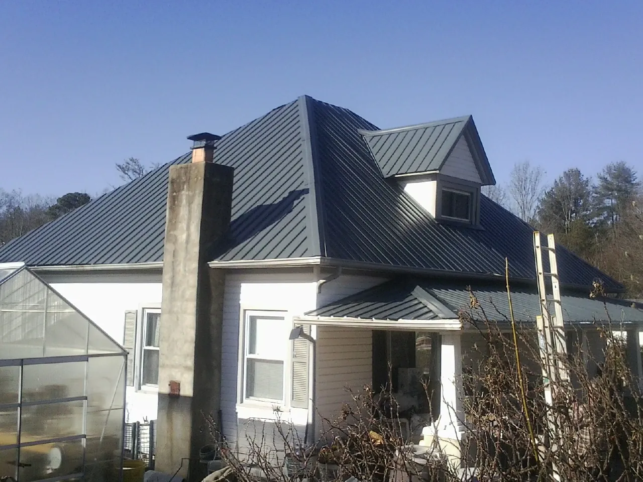 Dark blue standing seam metal roof on a white farmhouse with dormer — Slate & Tile Roof Repair by Roofing Brothers in Pena Blanca
