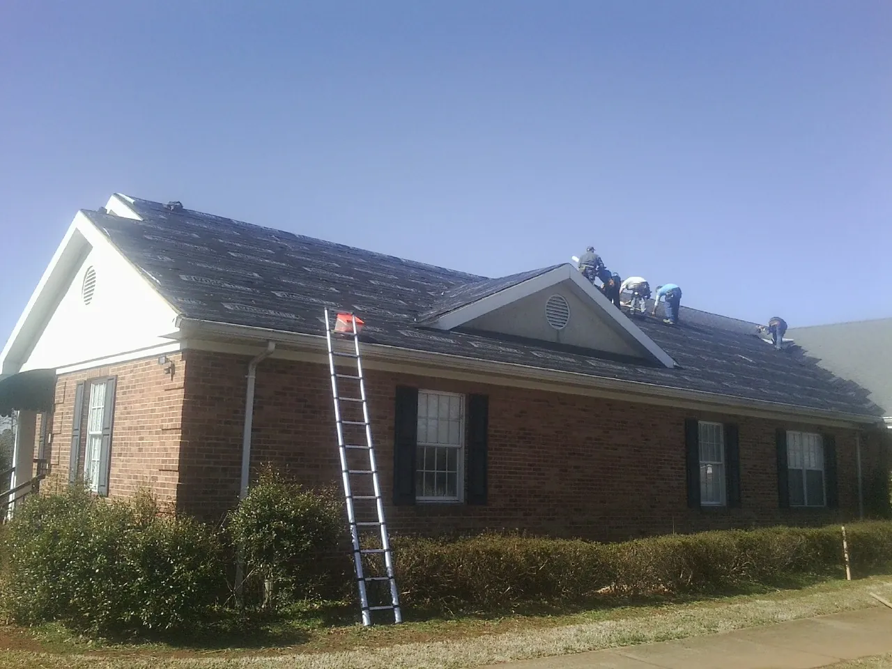 Crew tearing shingles off a brick ranch roof with a ladder set — Emergency Roof Repair work by our crew in Pena Blanca