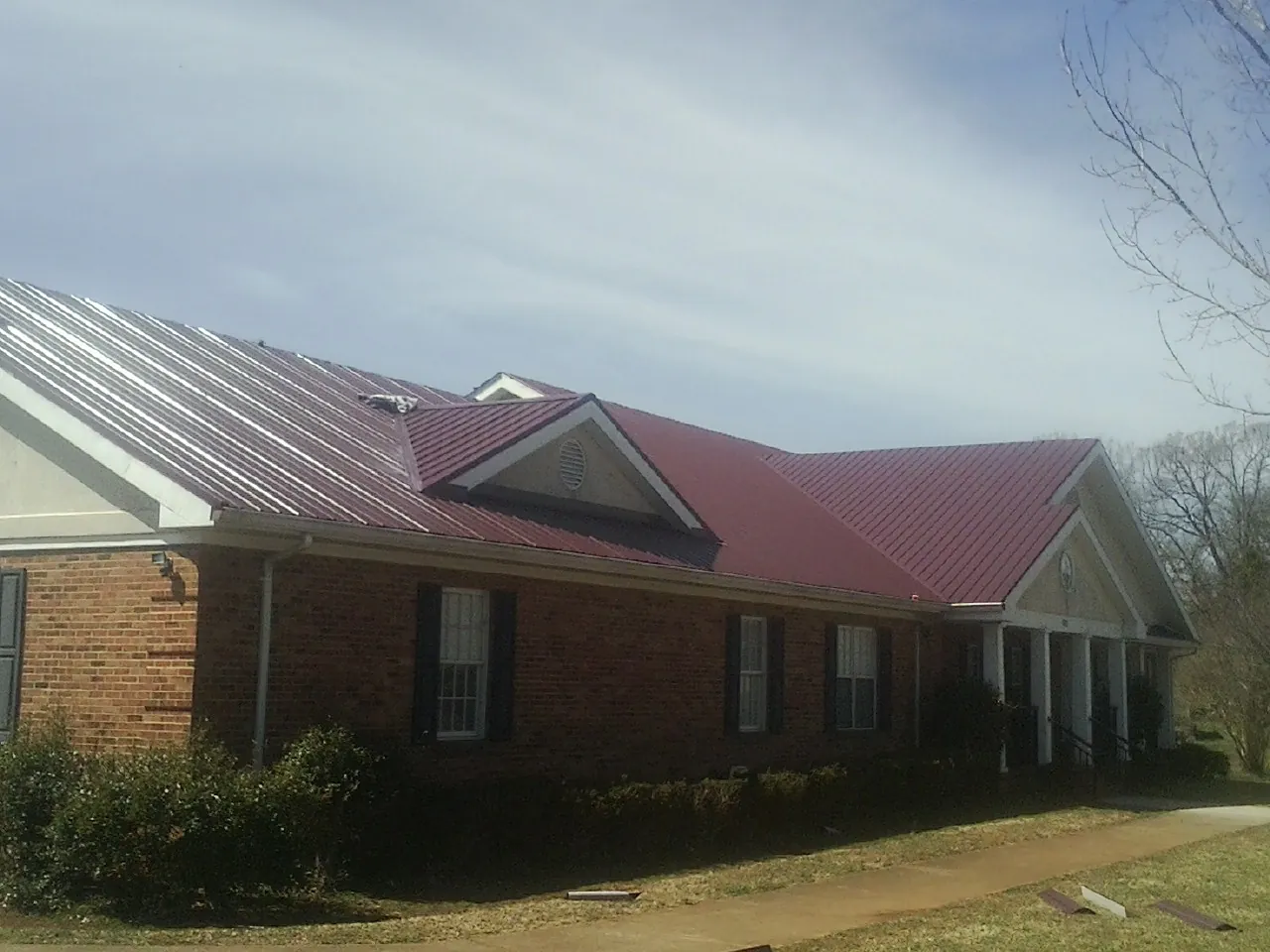 Red metal roof with gabled entries on a long brick building, from a Hail Damage Roof Repair job in Pena Blanca