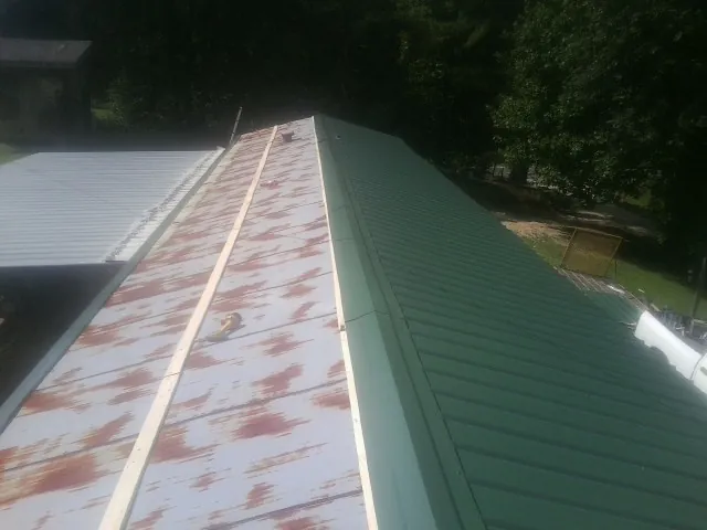 Old rusted panels beside newly installed green metal roofing — Wind Damage Roof Repair by Roofing Brothers in Pena Blanca