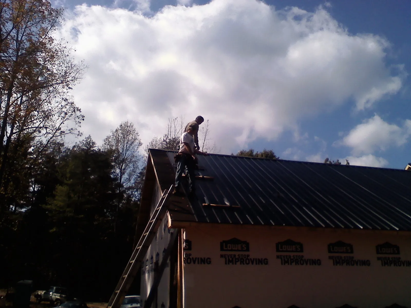Roofer fastening dark metal panels high against a cloudy sky, from a Roof Inspection job in Pena Blanca
