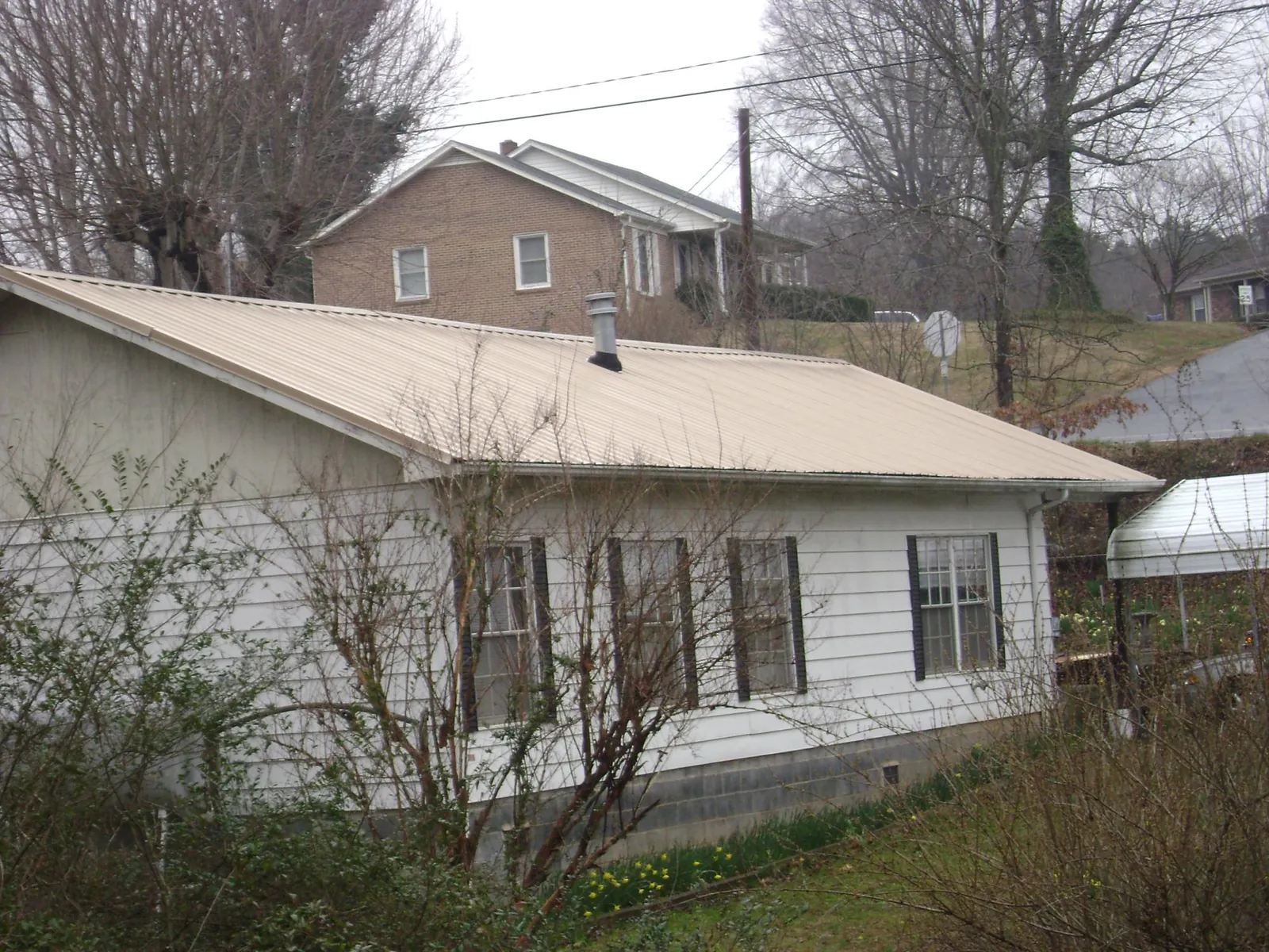 Tan metal roof on a white sided house set into a hillside — Commercial Roofing by Roofing Brothers in Pena Blanca