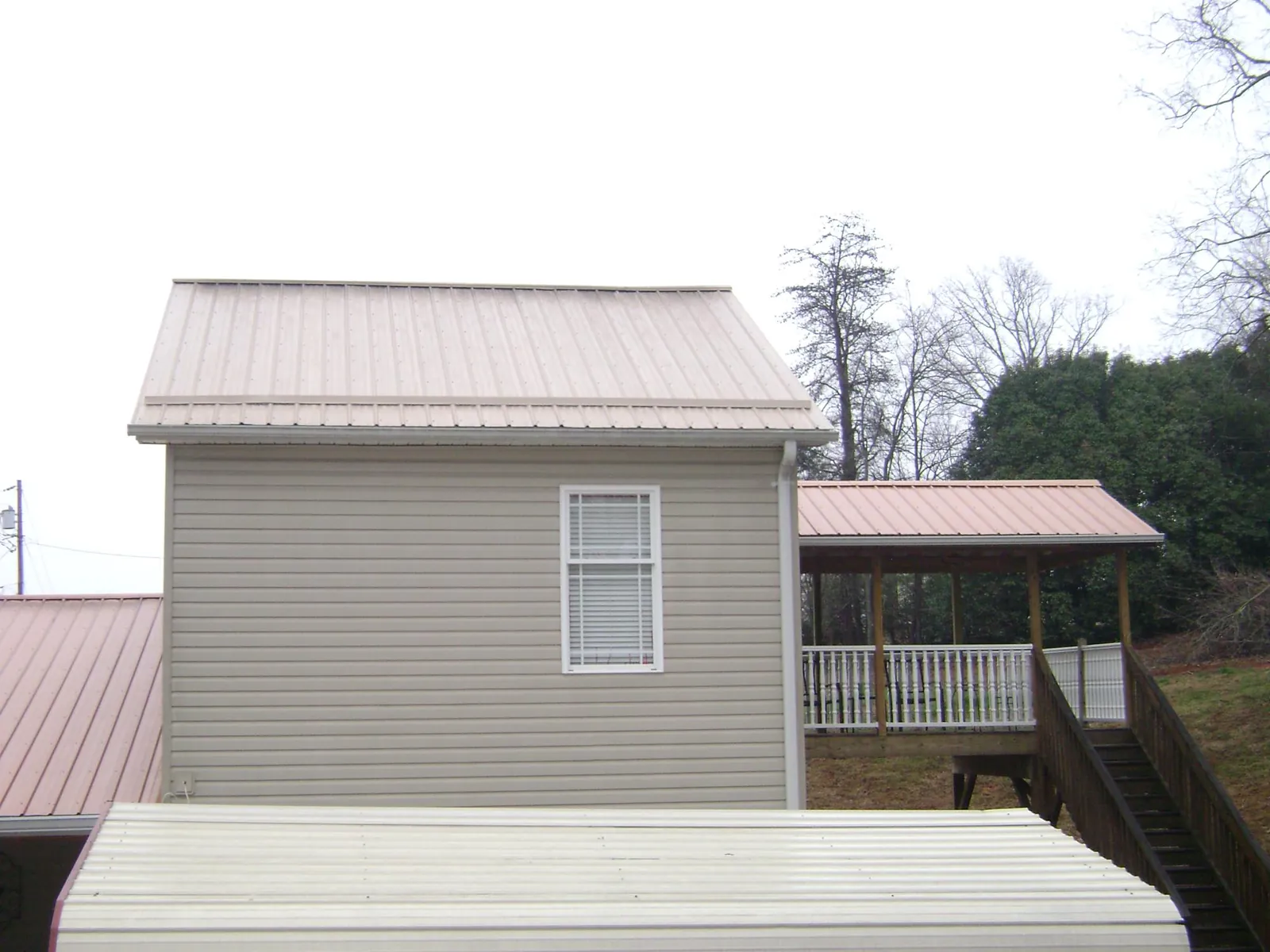 Tan metal roofs on a two story addition and attached porch, from a Roof Replacement job in Pena Blanca